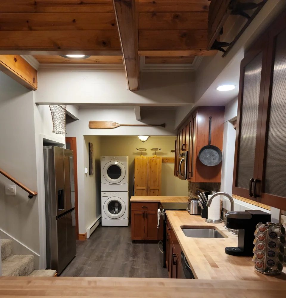 Cabin kitchen with wood countertops, cabinets and appliances, with a stacked washer and dryer at the far end.