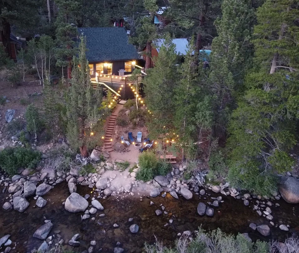 Tahoe River Cabin beside the Carson River at dusk, with a lit stairway leading to the riverside seating area.