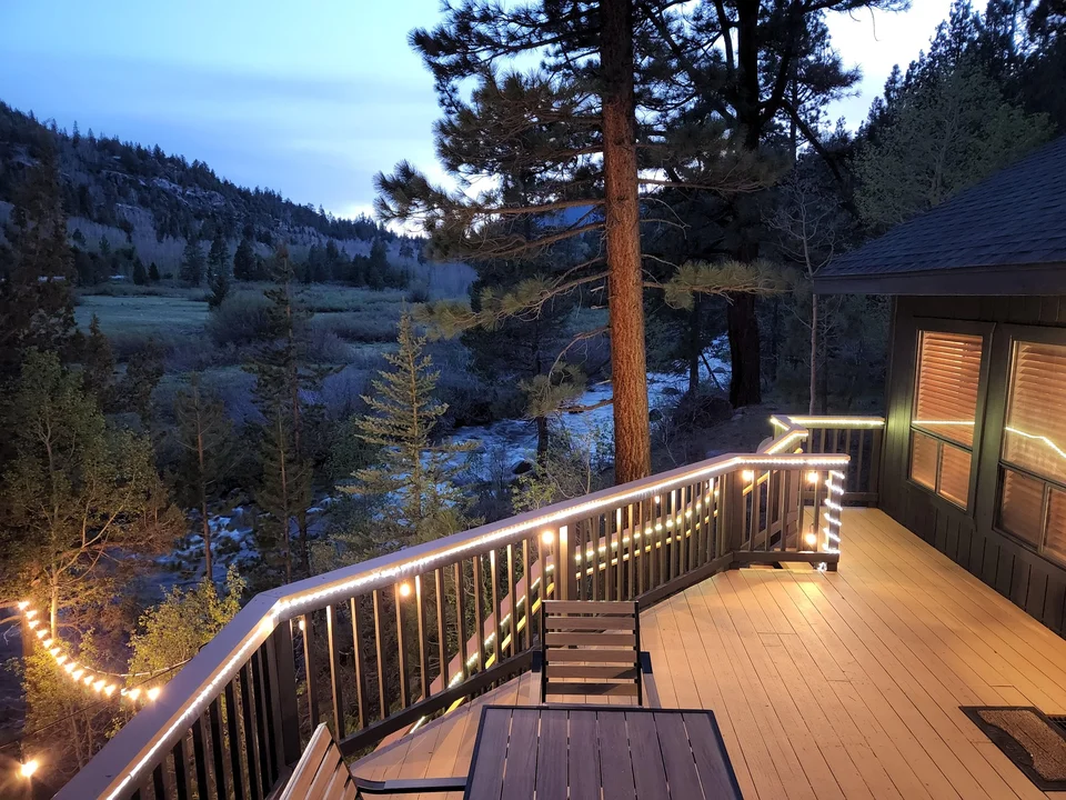 Illuminated cabin deck with an outdoor table, railing and views across Hope Valley at dusk.