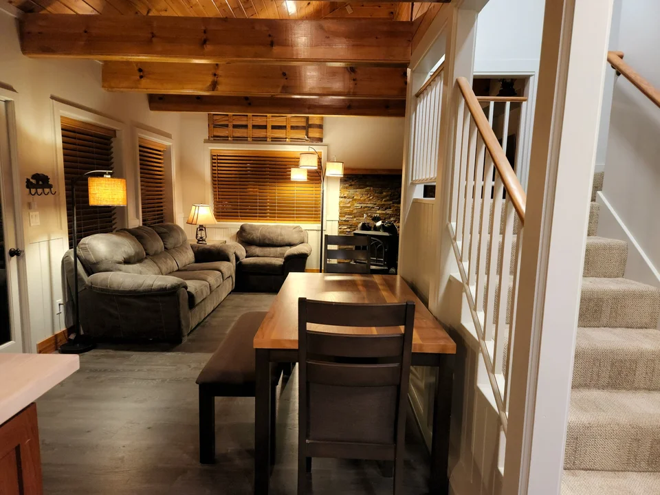 Dining table beside the staircase, with the cabin living room and wood stove beyond.