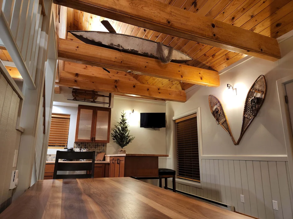 Rustic cabin dining area with exposed wood beams, a wooden table and decorative snowshoes on the wall.