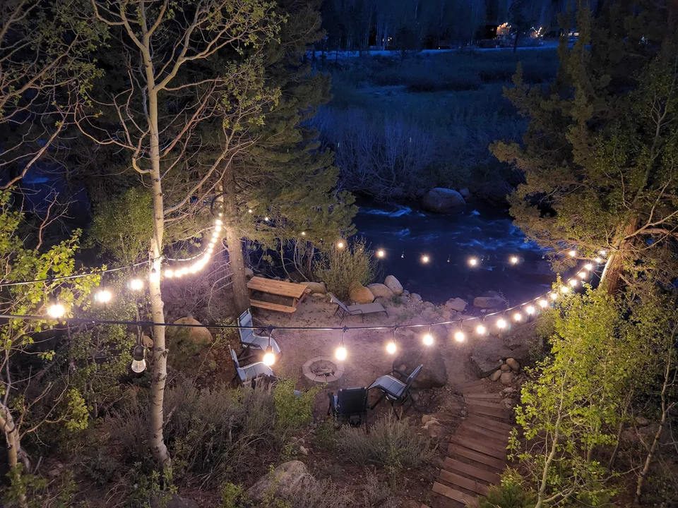 String lights illuminate the riverside seating area and stairs at Tahoe River Cabin after dark.