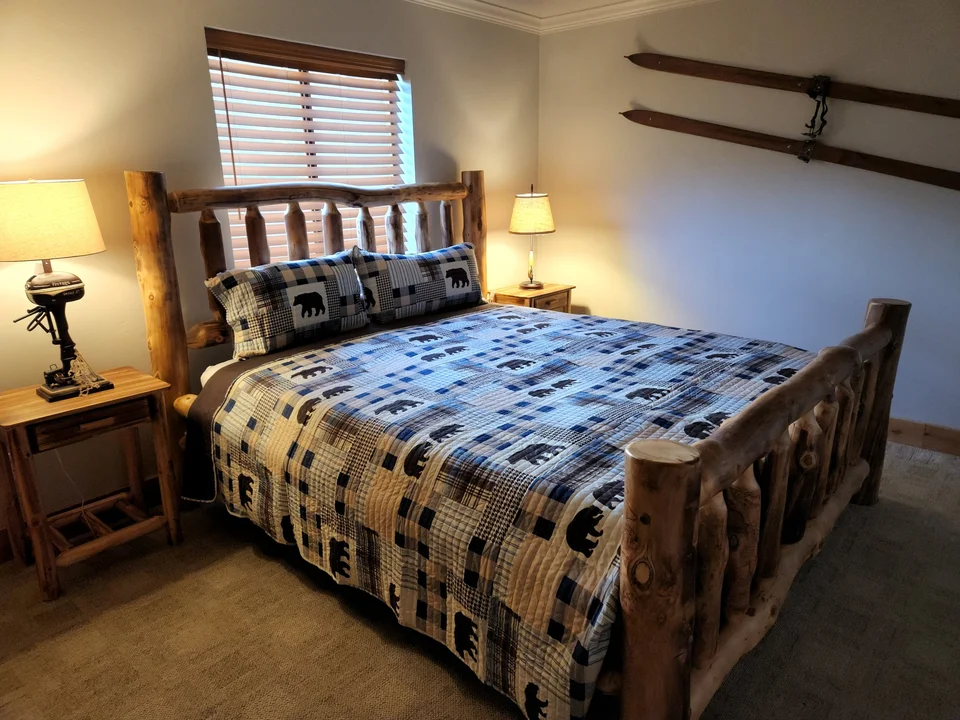 Cabin bedroom with a log-frame bed, patterned quilt, bedside tables and ski-themed wall decor.